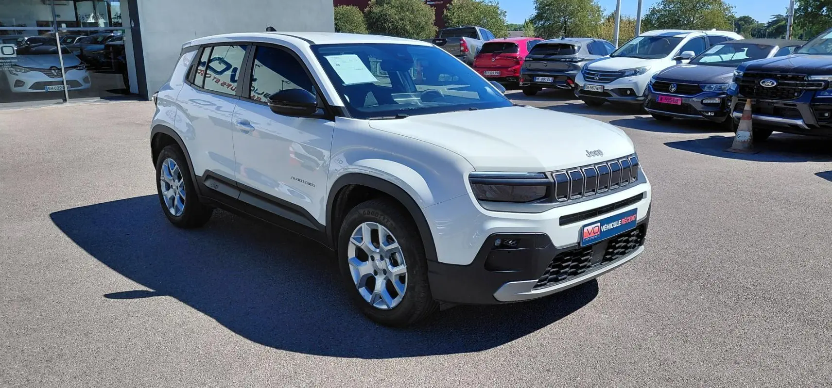 Jeep Avenger blanc en 3/4 avant droit, avec calandre distinctive et jantes alliage, stationné en extérieur.