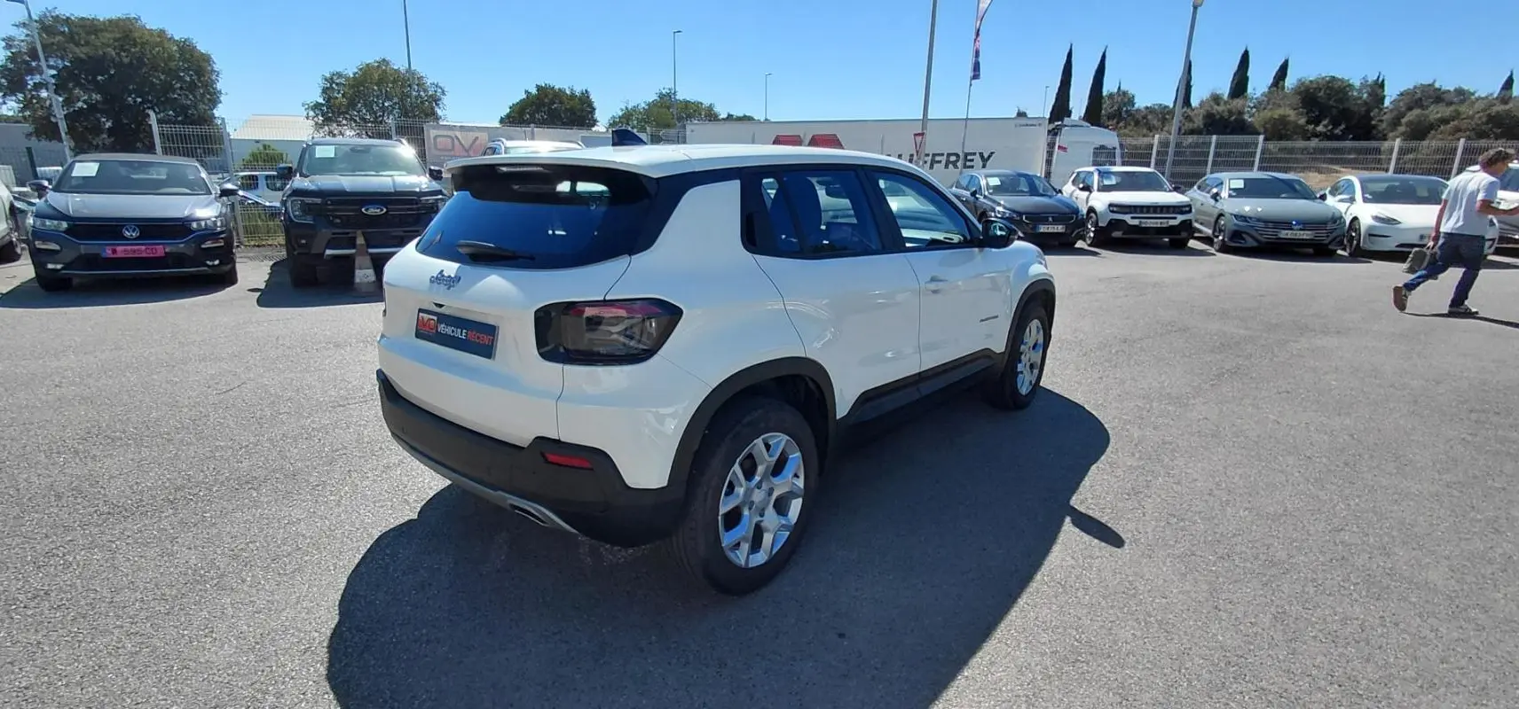 Jeep Avenger blanc vu en 3/4 arrière droit sur un parking, avec des jantes alliage et des feux arrière fumés.