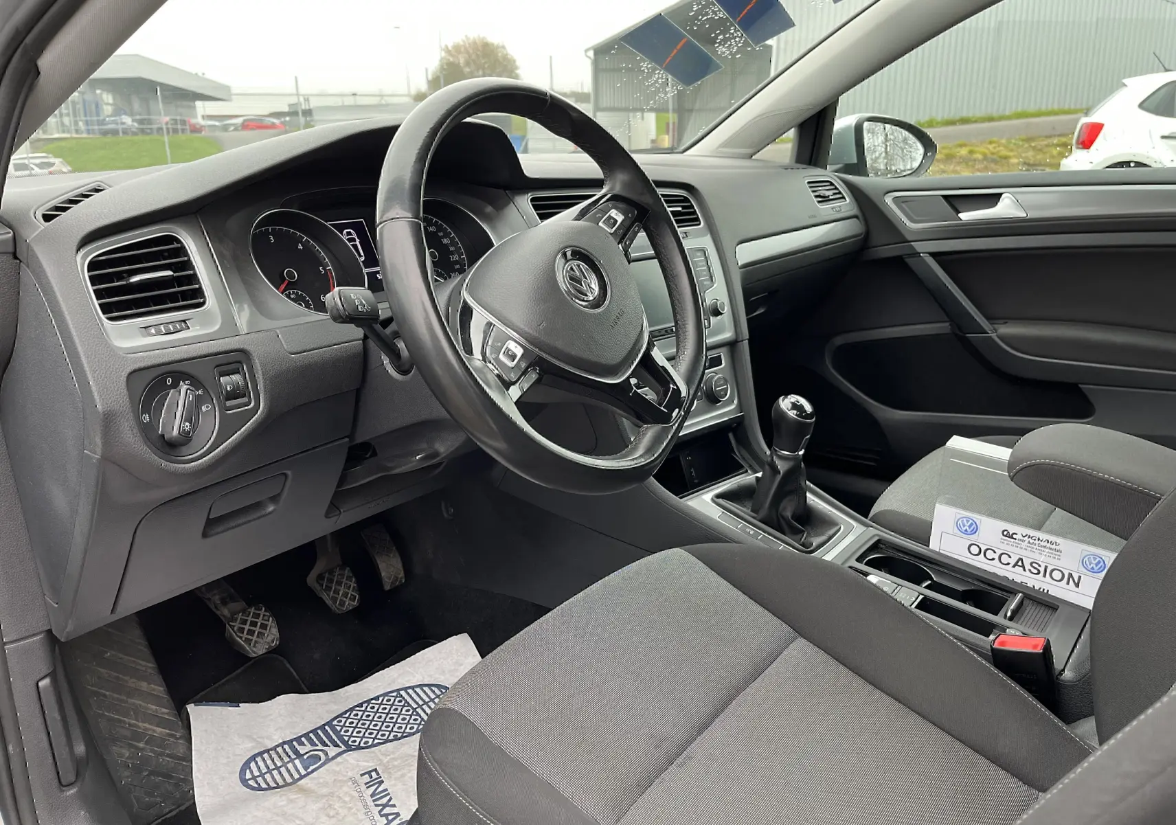 Intérieur noir de Volkswagen Golf 7 2017, vue côté conducteur montrant volant, tableau de bord et levier de vitesse manuel.