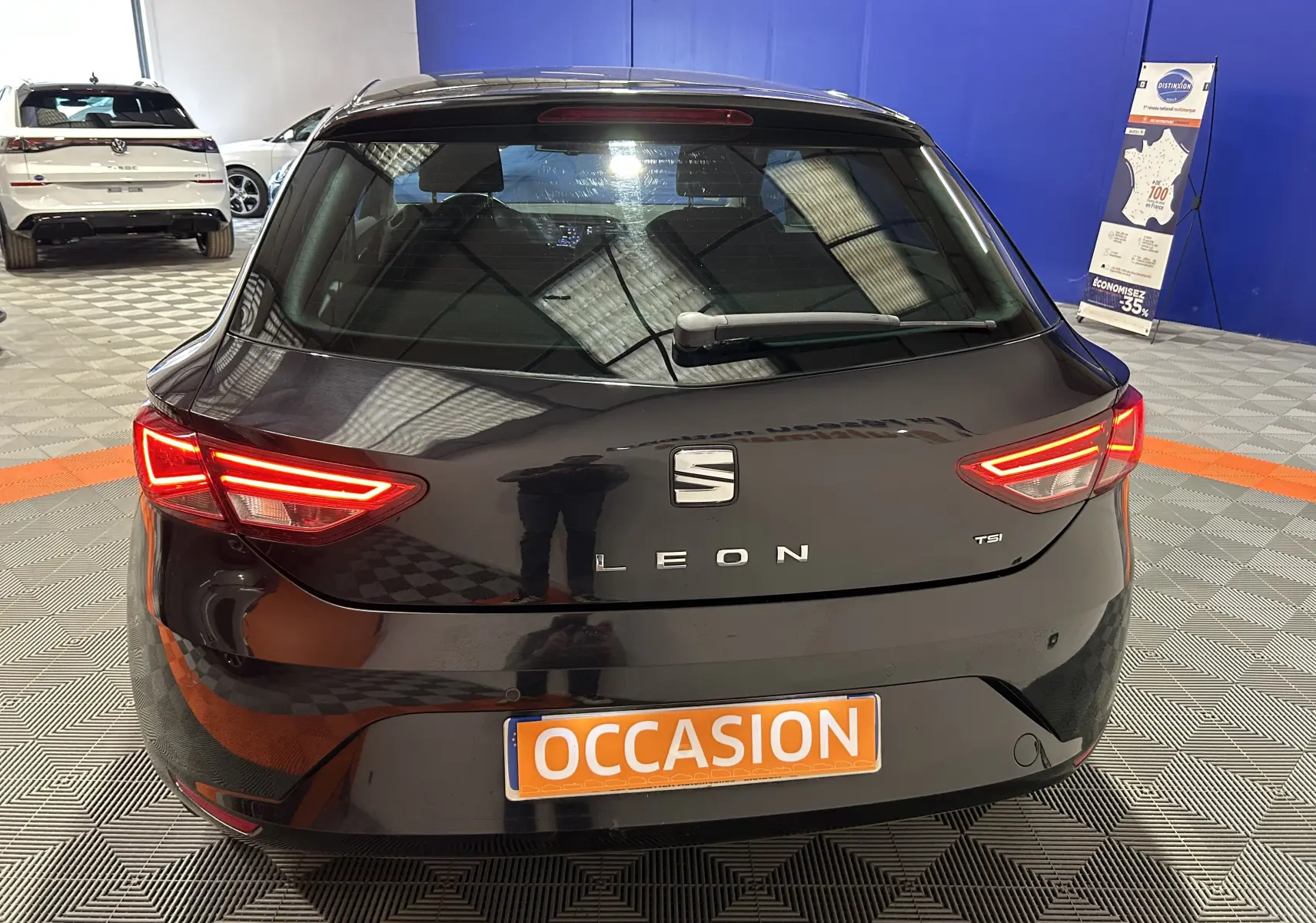 Vue arrière d'une SEAT Leon noire de 2014 avec feux allumés, plaque "OCCASION" en intérieur de showroom.
