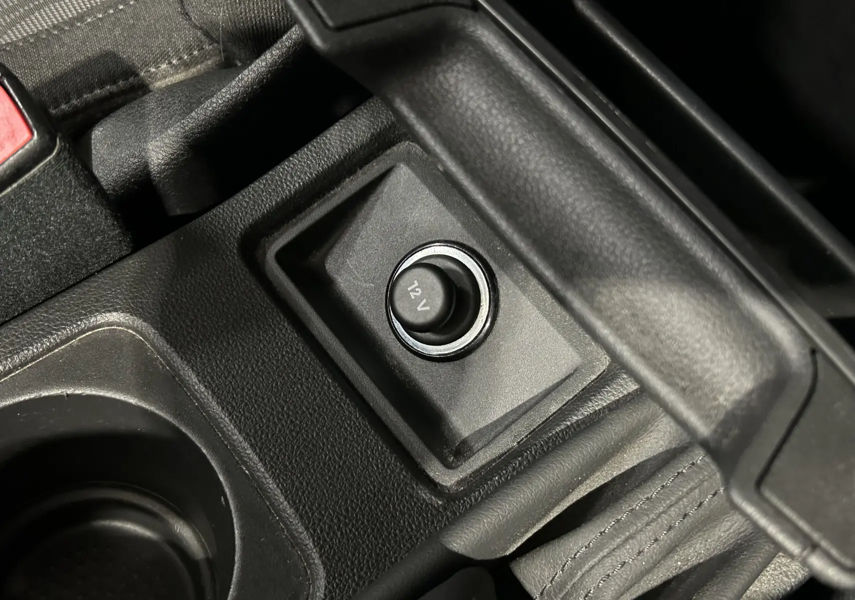 Gros plan sur la prise 12V noire située entre le frein à main et le porte-gobelet dans l’habitacle d’une SEAT Leon noire.