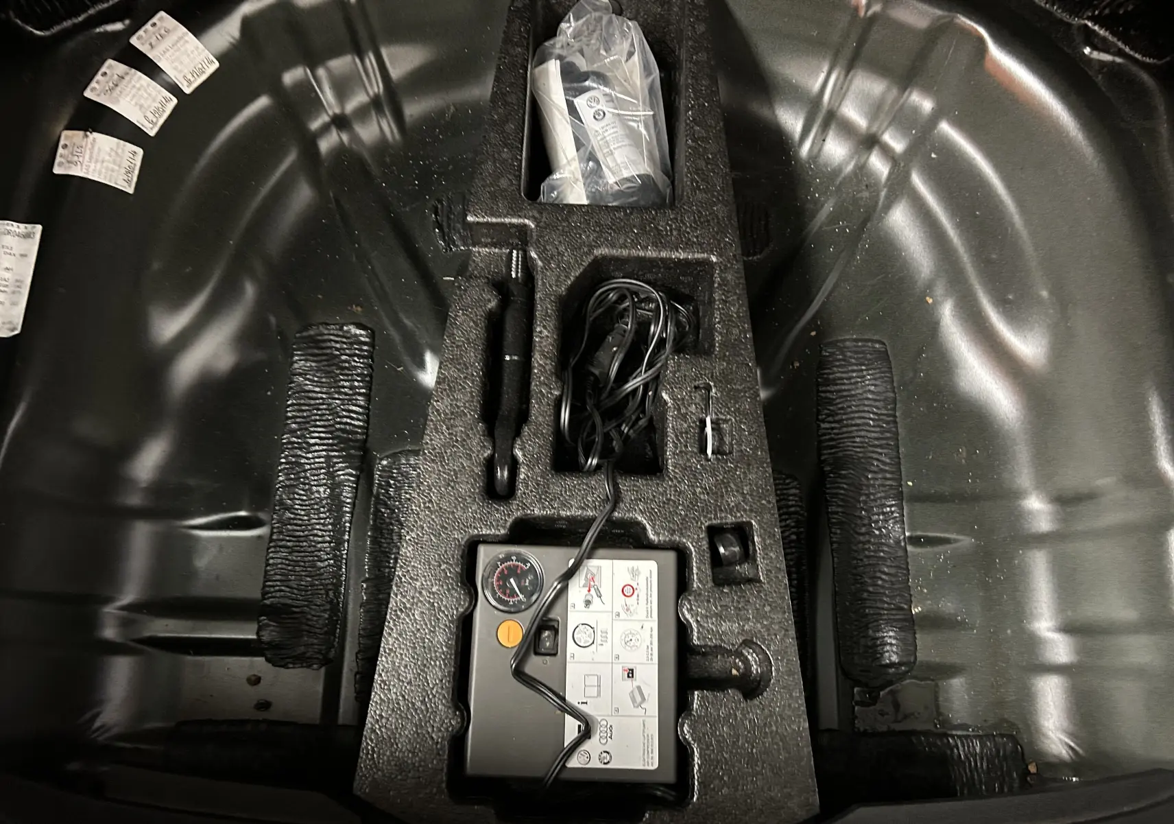 Vue plongeante sur le compartiment de roue de secours d'une SEAT Leon noire avec kit de réparation et accessoires rangés.