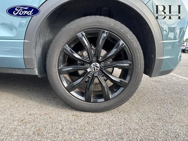 Gros plan sur la roue avant gauche noire brillante d'un Volkswagen T-Roc bleu pétrole métallisé.