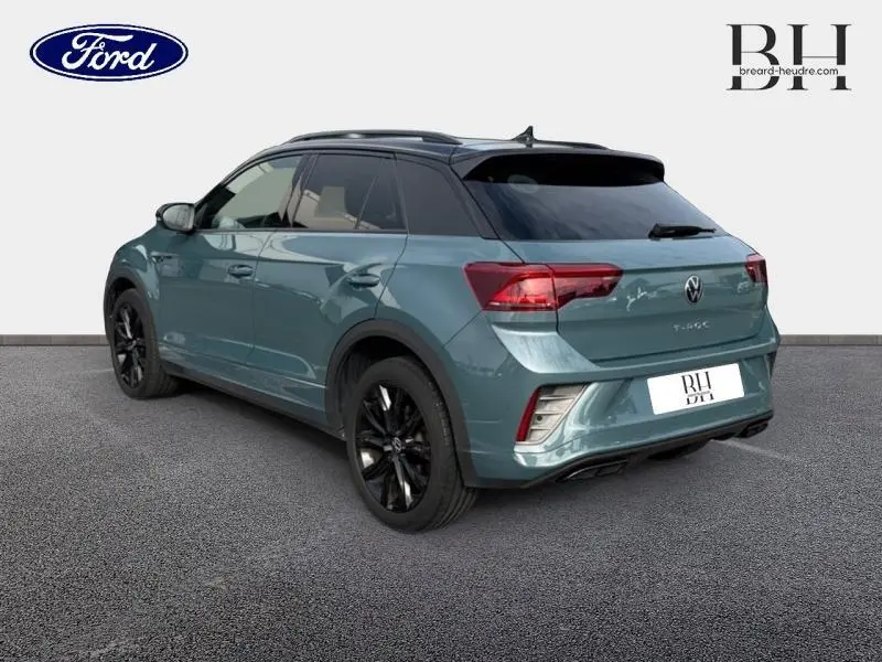 Volkswagen T-Roc bleu pétrole métallisé vu en 3/4 arrière droit avec jantes noires et toit noir.