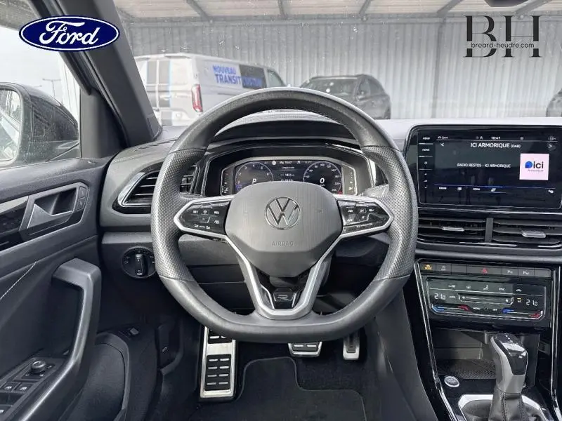 Vue intérieure centrée sur le volant cuir multifonction d'un Volkswagen T-Roc 1.5 TSI R-Line avec tableau de bord numérique.