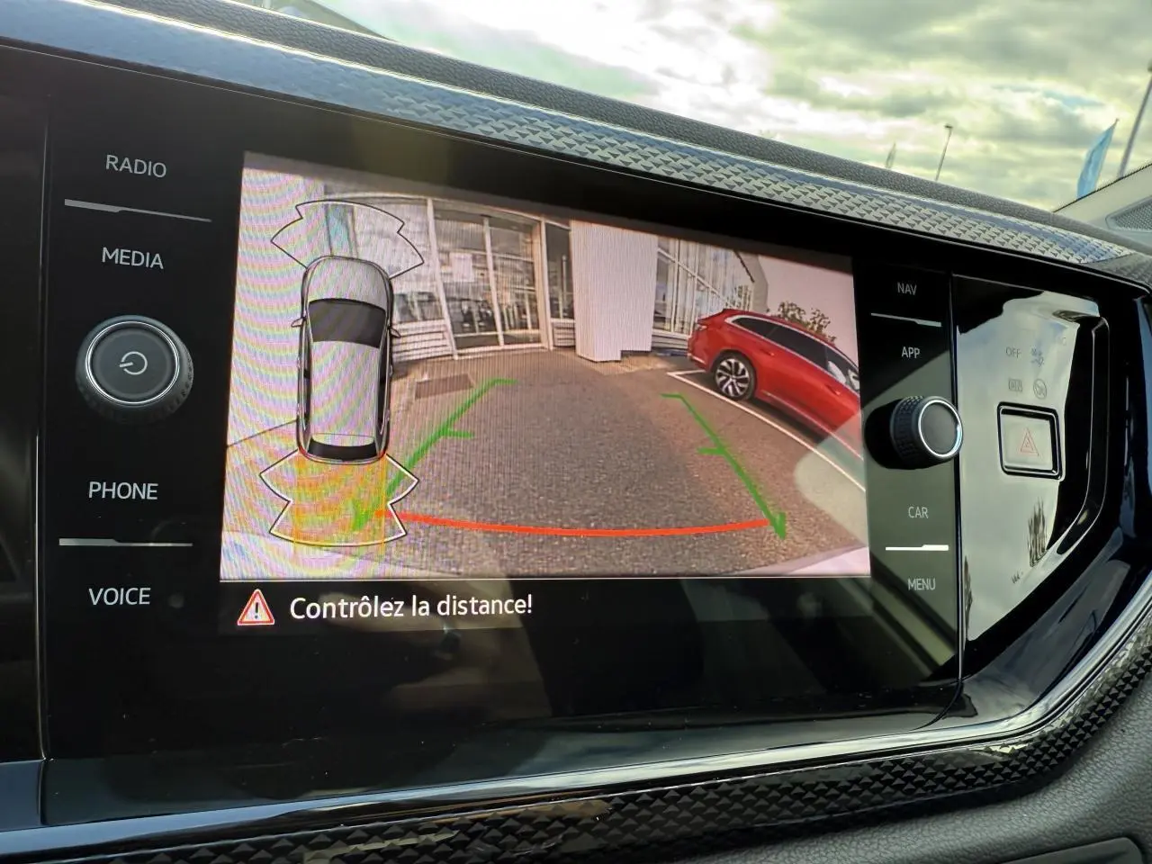 Affichage de la caméra de recul sur l'écran multimédia d'une Volkswagen Polo gris reflet argent avec un véhicule rouge en arrière-plan.