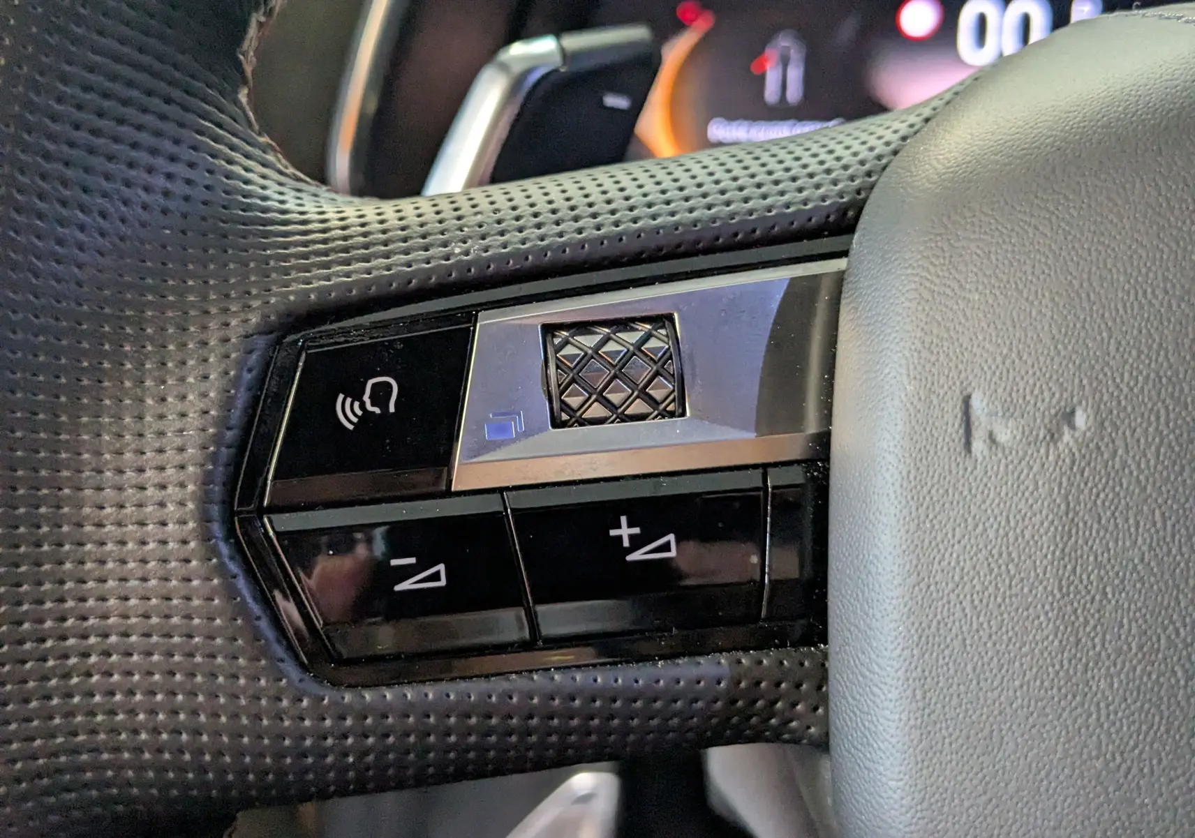 Gros plan sur les commandes au volant côté gauche du DS7 gris laqué, avec boutons de volume et fonction mains libres.