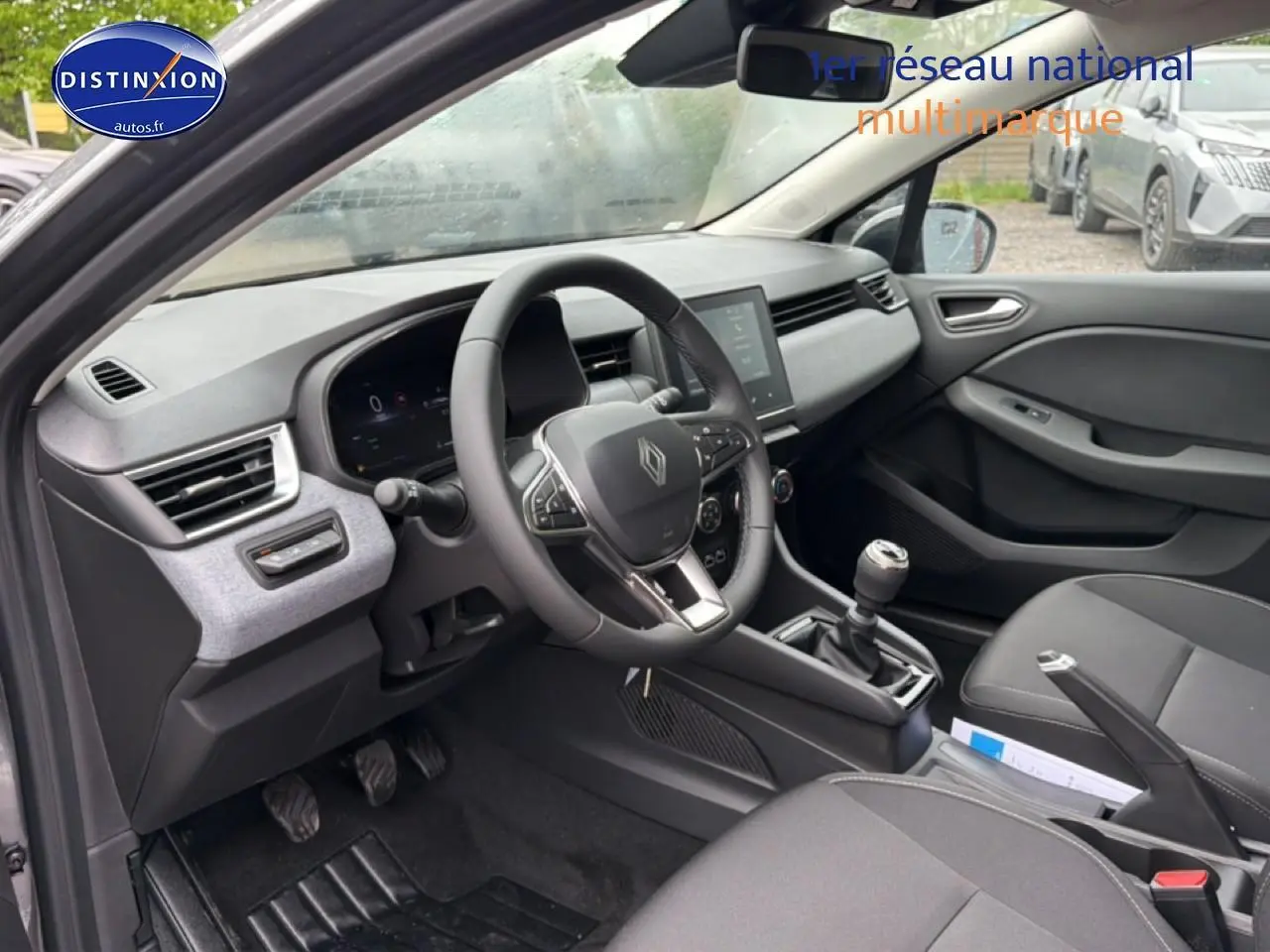 Vue intérieure côté conducteur de la Renault Clio V gris schiste, avec volant multifonction et boîte manuelle visible.
