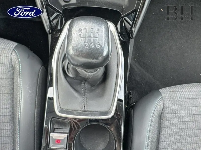 Le levier de vitesses manuel noir entouré de la console centrale brillante, entre deux sièges tissu gris.