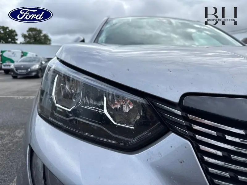 Gros plan sur le phare avant gauche d'une Peugeot 2008 gris Artense, soulignant la calandre et les lignes du capot.