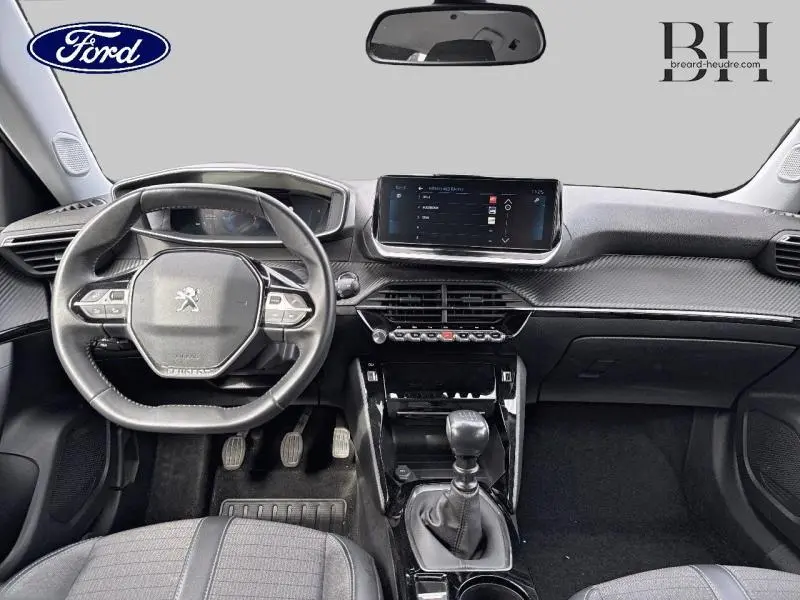 Vue intérieure avant du tableau de bord et volant d'une Peugeot 2008 gris Artense avec boîte manuelle et écran tactile central.