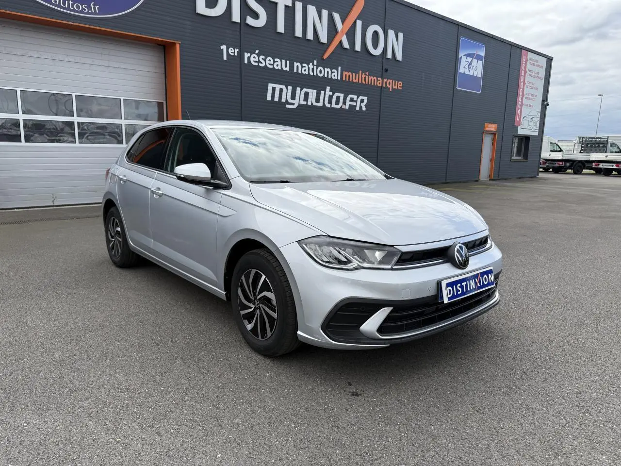 Volkswagen Polo 2025 gris reflet argent vue 3/4 avant avec jantes alliage et calandre noire devant un garage.