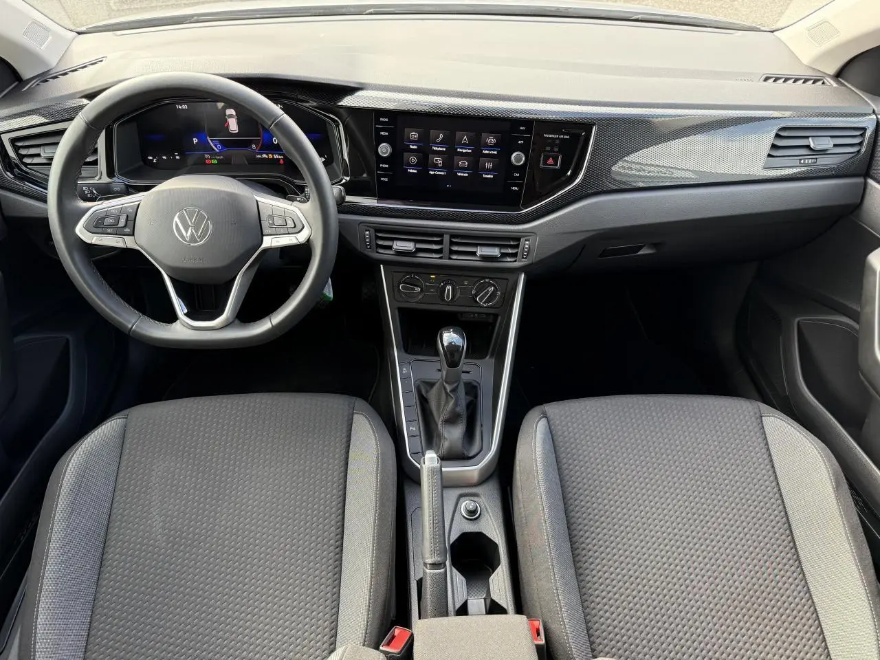 Vue intérieure avant du tableau de bord et des sièges gris de la Volkswagen Polo 2025 avec écran tactile et volant multifonction.