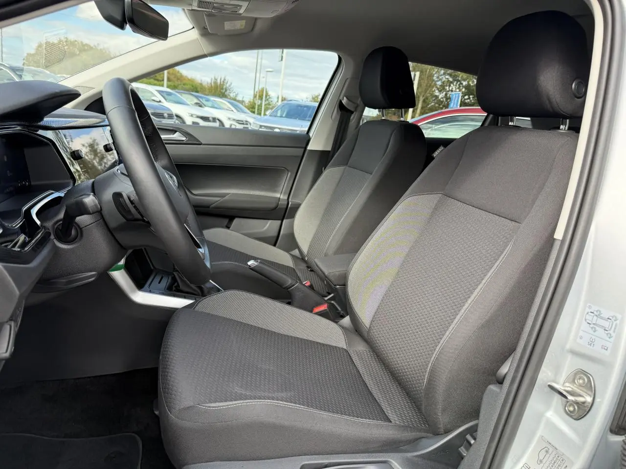 Vue intérieure côté conducteur de la Volkswagen Polo gris Reflet Argent, sièges tissu gris et tableau de bord moderne.