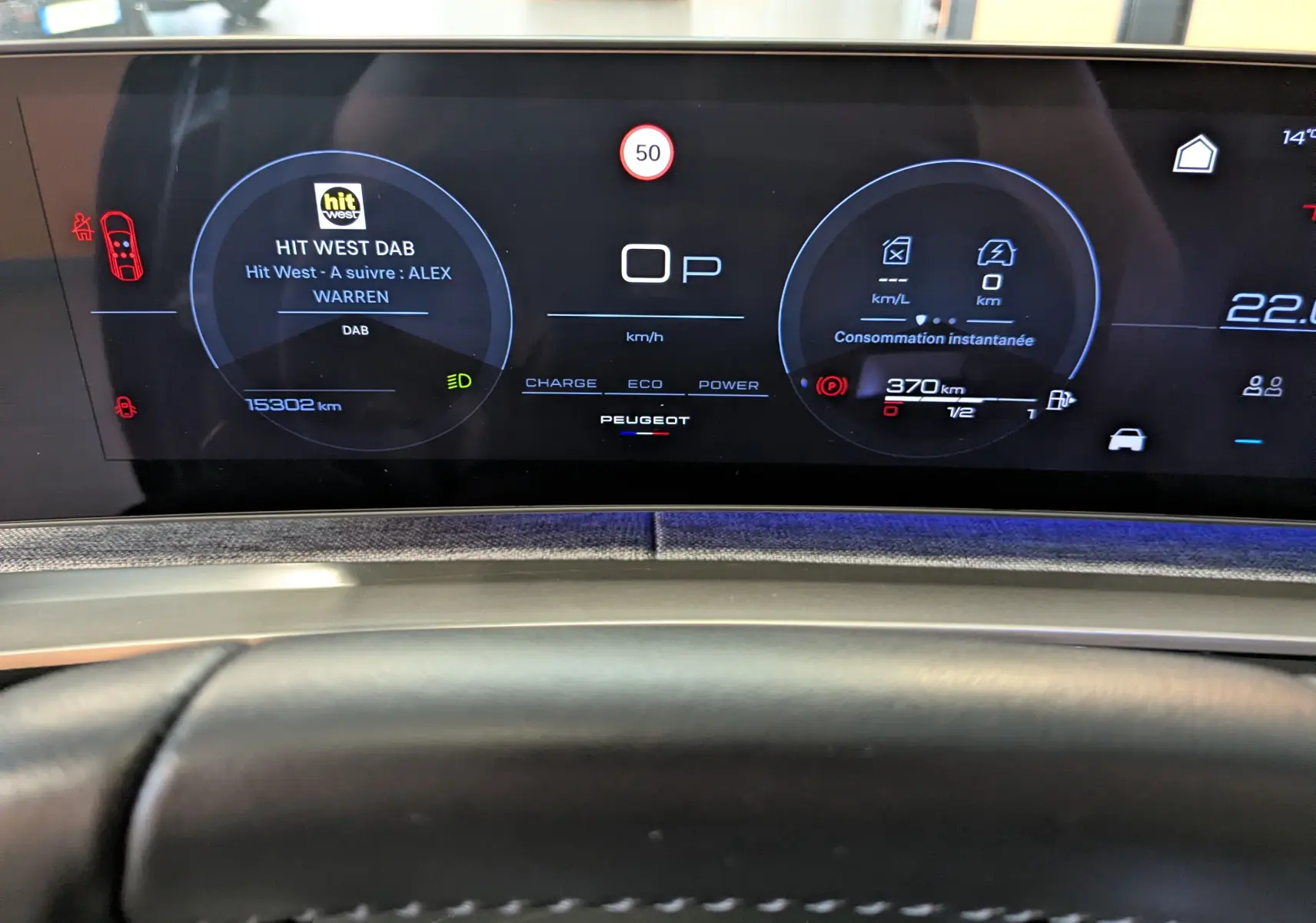 Vue rapprochée du tableau de bord numérique du Peugeot 3008 Hybrid 145 noir, affichant la radio et l'autonomie restante.