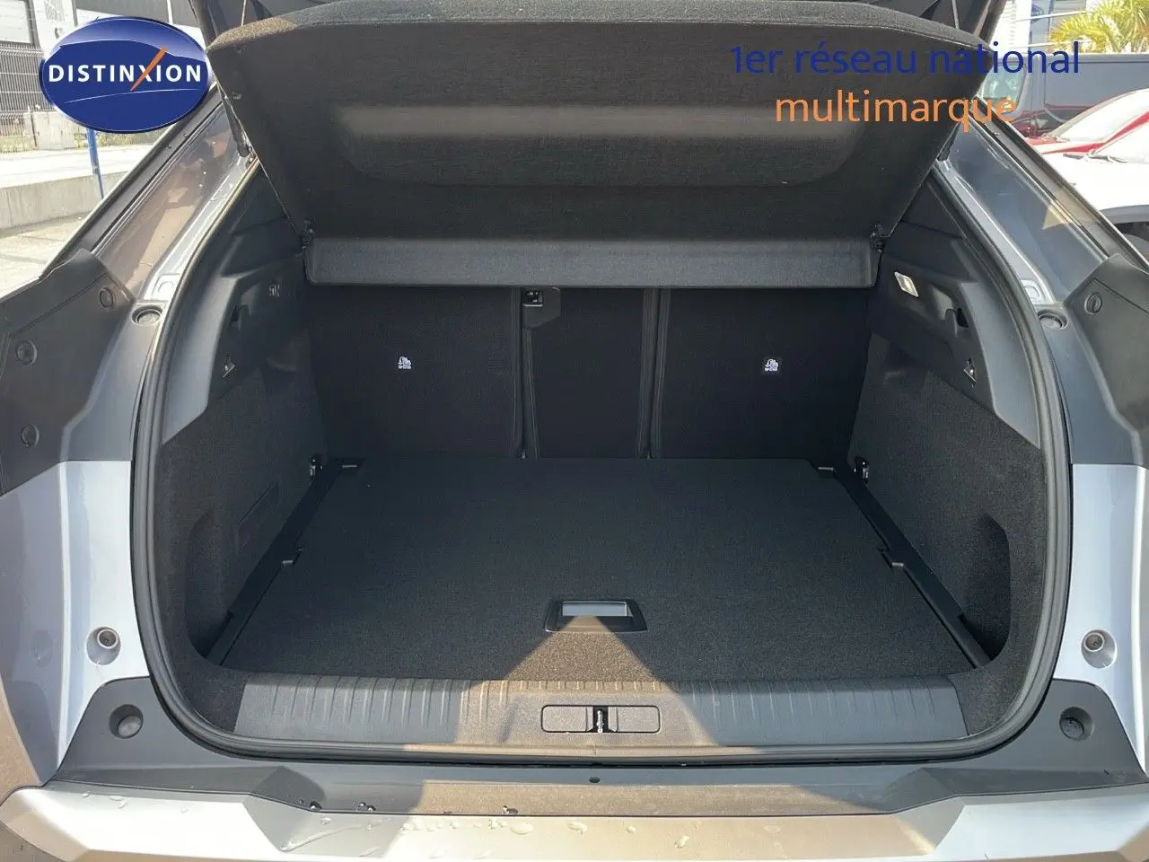 Coffre ouvert vu de l'arrière d'un Peugeot 3008 Hybrid gris Artense métal, montrant un espace de chargement vide.