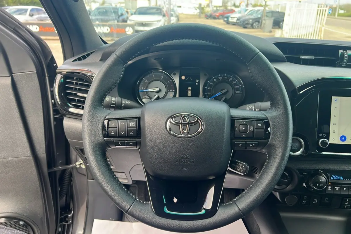 Vue intérieure centrée sur le volant du Toyota Hilux 2025 gris atlas, avec tableau de bord et commandes visibles.