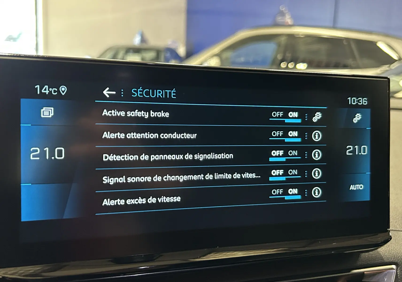 Écran tactile intérieur du Peugeot 5008 2024 affichant les réglages de sécurité avec un SUV gris en arrière-plan flou.