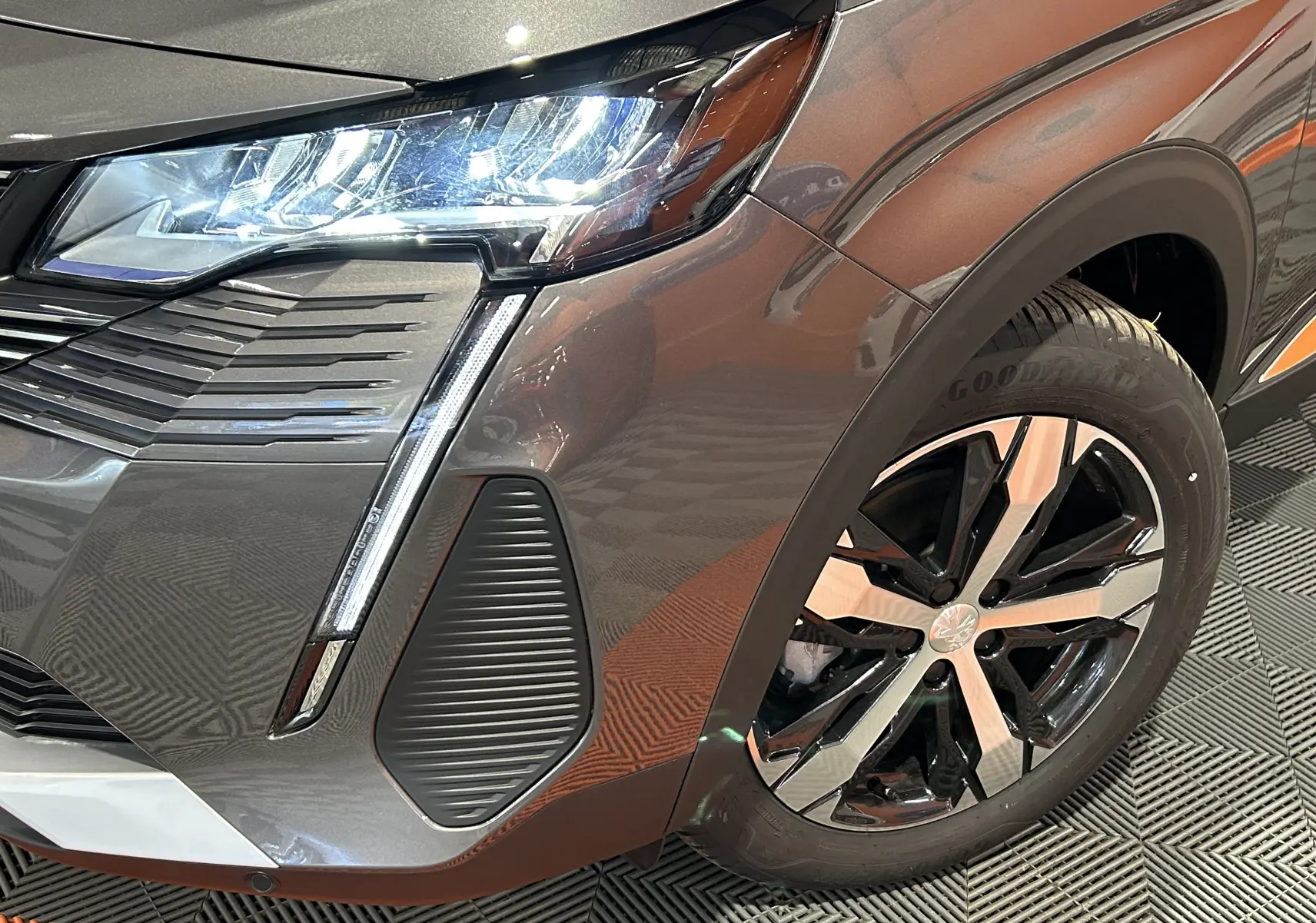 Gros plan sur l'avant droit du Peugeot 5008 gris Platinium, mettant en valeur le phare LED et la roue au design bicolore.