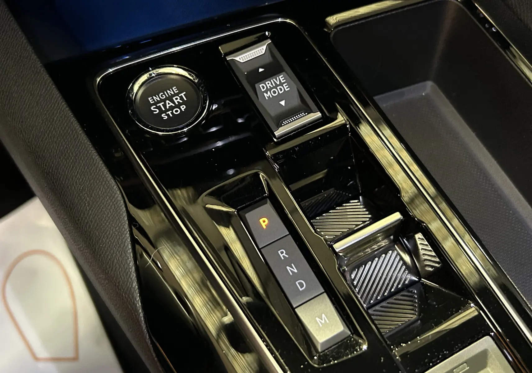 Gros plan sur la console centrale noire brillante du Peugeot 5008 2024 avec bouton start/stop et sélecteur de mode de conduite.