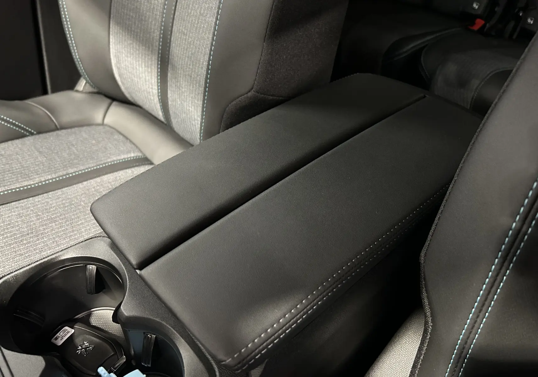 Accoudoir central noir avec surpiqûres bleues entre les sièges avant du Peugeot 5008 Gris Platinium 2024.