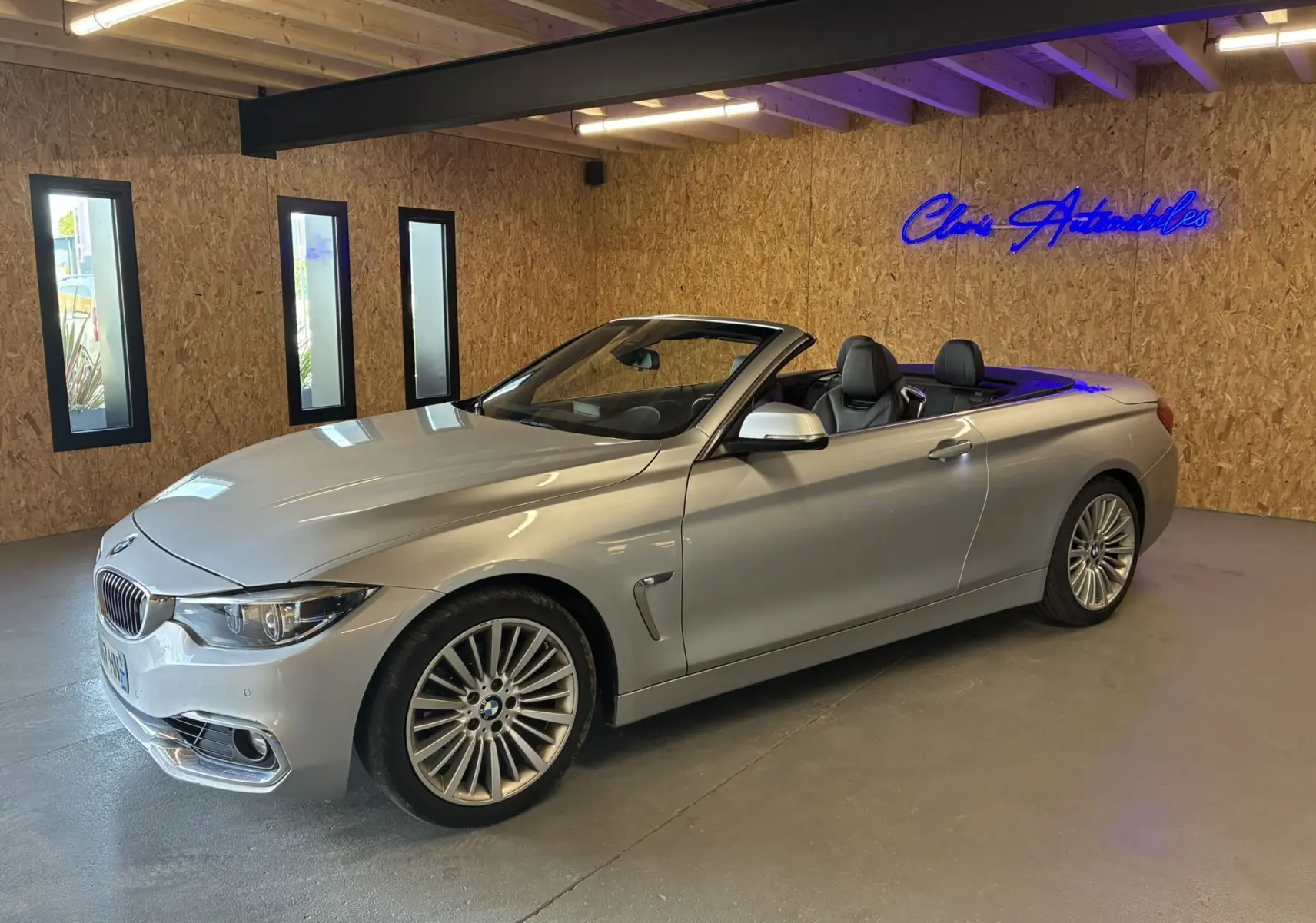 BMW Série 4 Cabriolet gris vue 3/4 avant droit, capote ouverte, intérieur cuir noir visible en showroom.