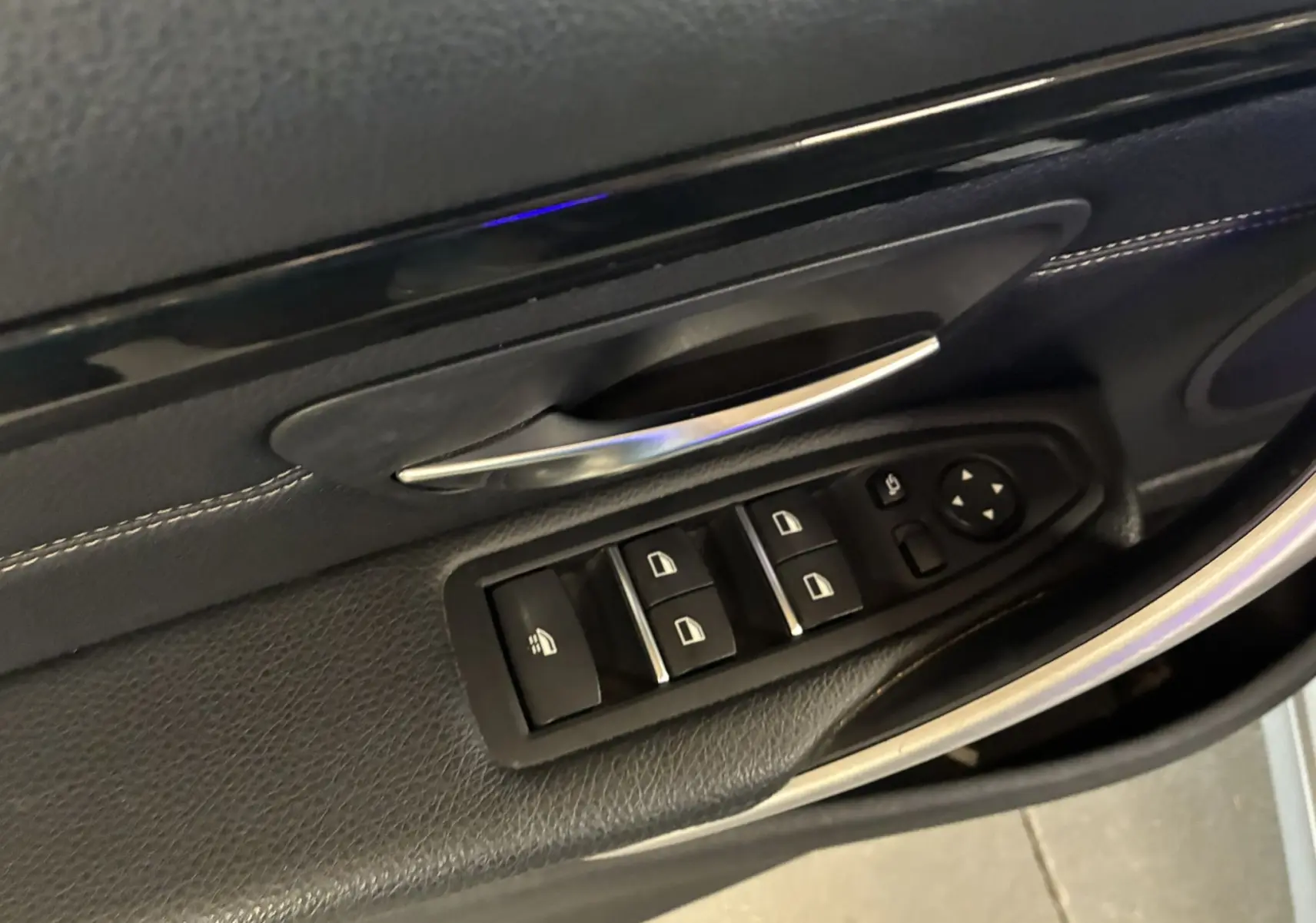 Gros plan sur la commande des vitres et la poignée de porte côté conducteur en cuir noir d'une BMW Série 4 Cabriolet gris 2019.