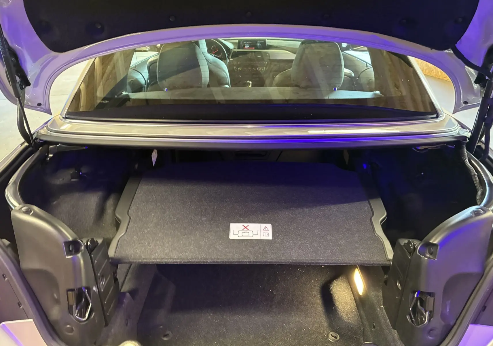 Coffre ouvert vu de l'arrière d'une BMW Série 4 Cabriolet gris avec intérieur noir et banquette arrière visible.