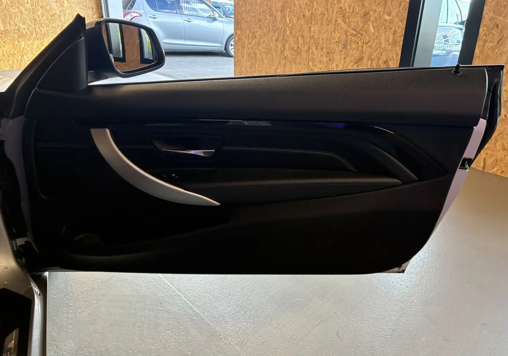 Vue rapprochée de la porte côté gauche ouverte d'une BMW Série 4 Cabriolet gris, intérieur noir avec poignée argentée.