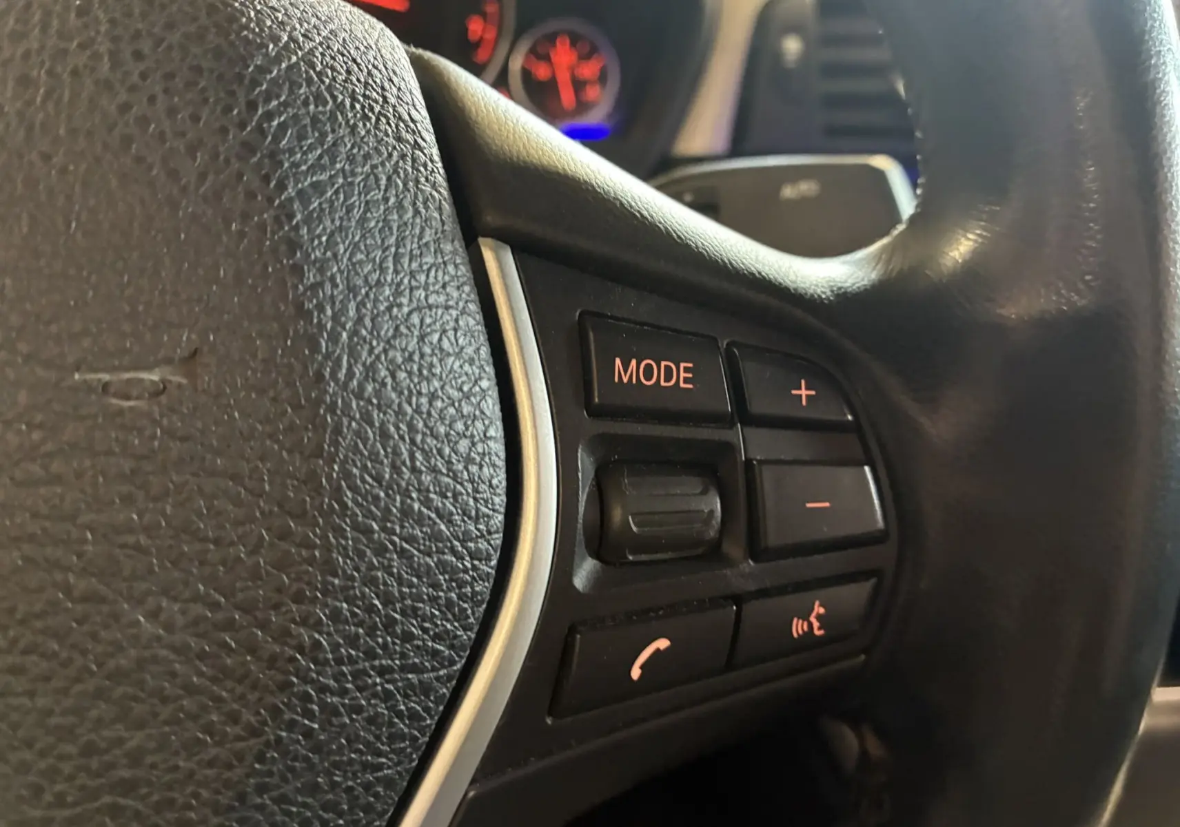 Gros plan sur les commandes du volant en cuir noir d'une BMW Série 4 Cabriolet gris, avec boutons mode et volume.