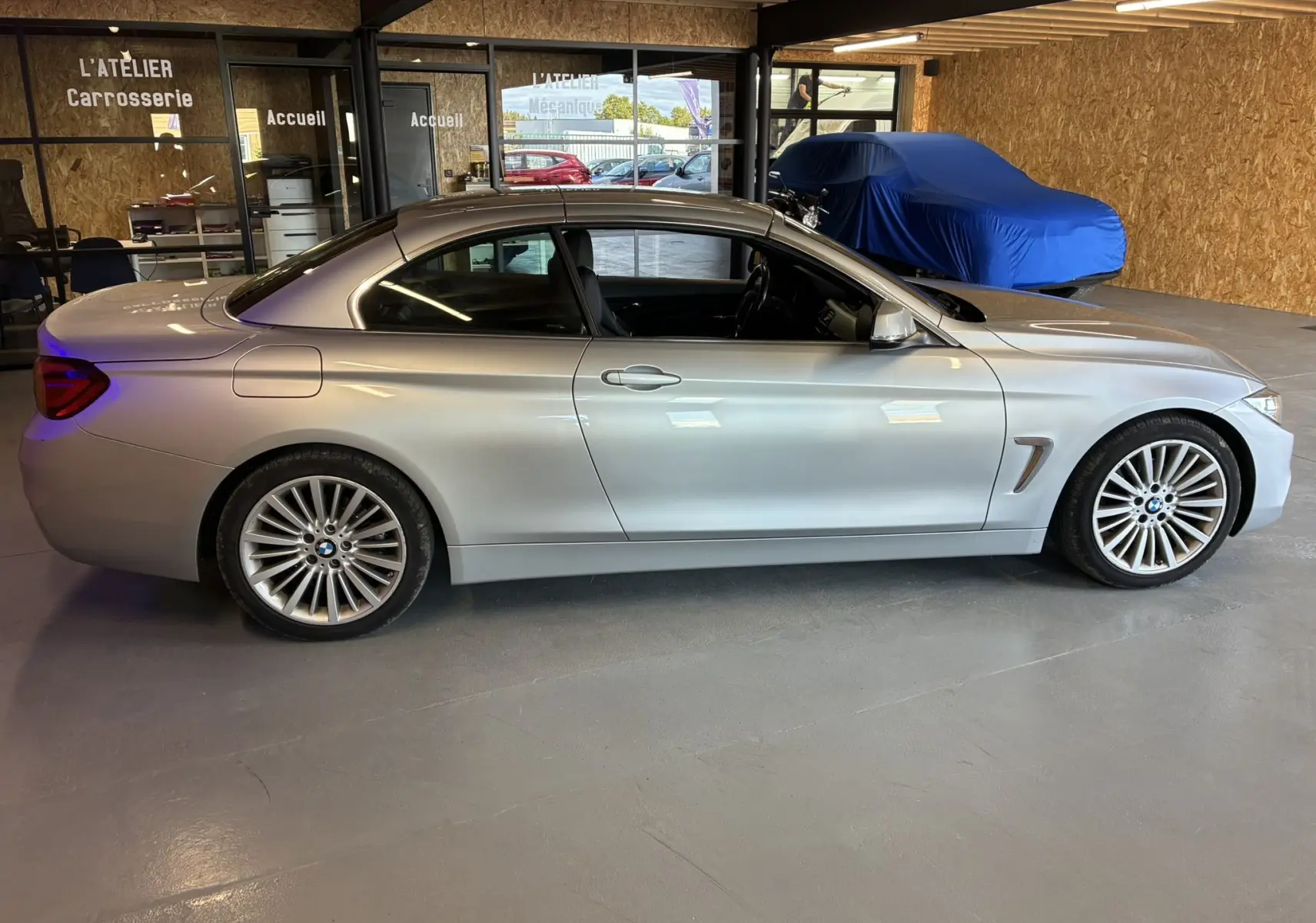 BMW Série 4 Cabriolet 420i gris vue de profil côté gauche dans un atelier avec intérieur noir visible