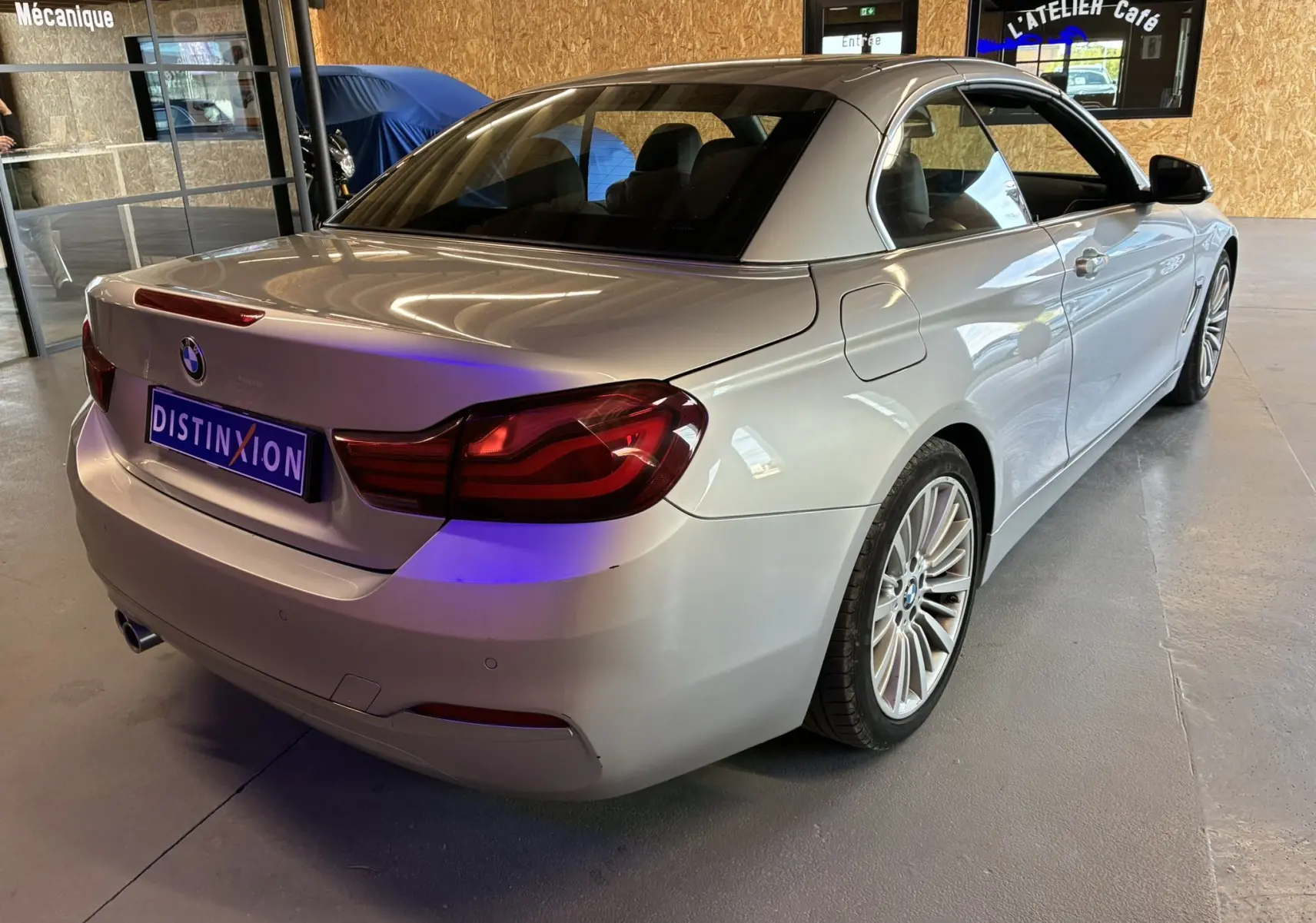 BMW Série 4 Cabriolet gris vue 3/4 arrière droit, toit rigide fermé, jantes multi-branches en intérieur d'atelier.