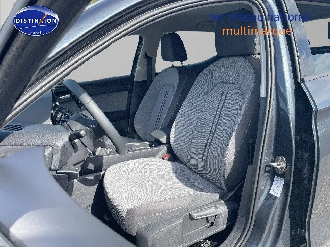 Vue intérieure côté conducteur du SEAT LEON gris magnétique métal, mettant en valeur les sièges en tissu gris clair et noir.