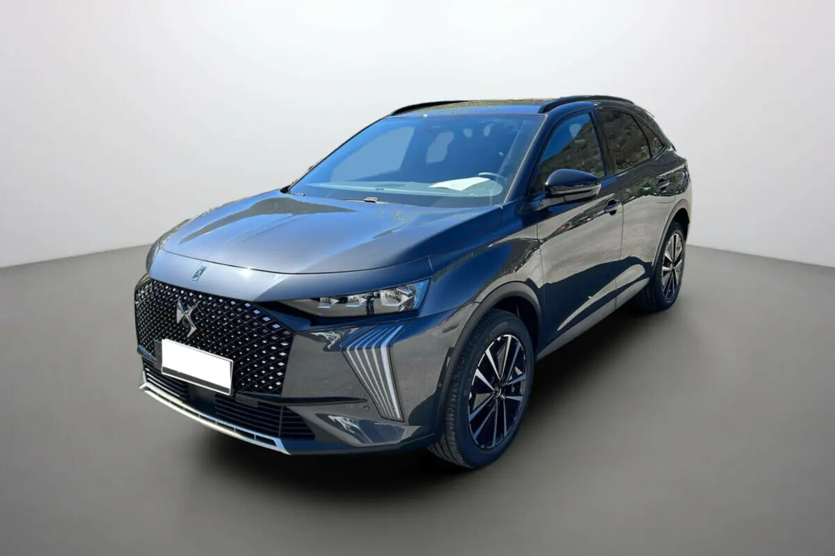 DS7 gris titane en 3/4 avant droit, avec calandre distinctive et jantes noires à motifs modernes.