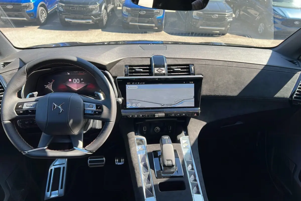 Vue intérieure avant du DS7 2025 gris titane, mettant en valeur le volant multifonction et l'écran tactile central large.