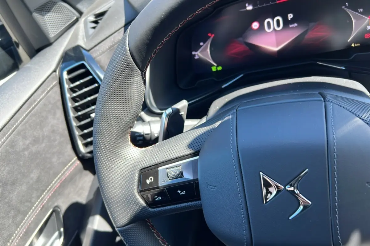 Gros plan sur le volant en cuir perforé du DS7 2025 gris titane, avec commandes intégrées et tableau de bord numérique.
