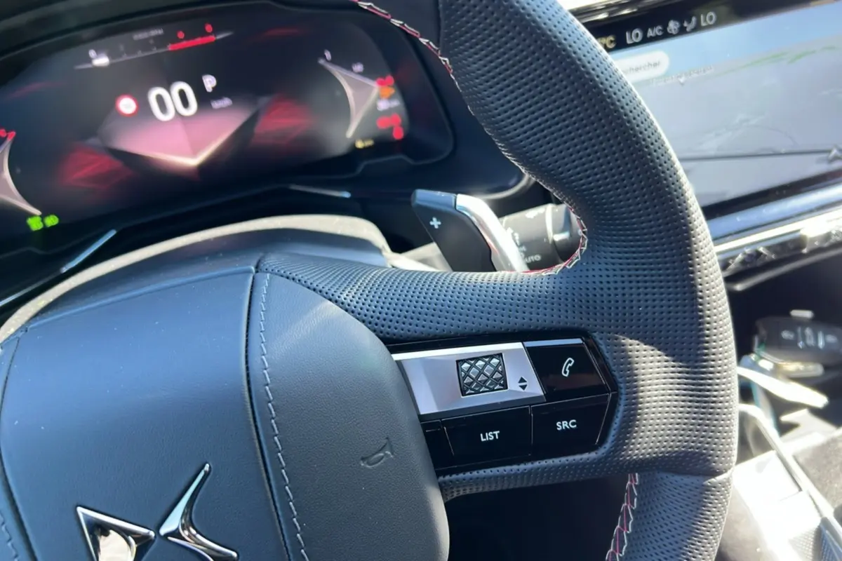 Gros plan sur le volant perforé et les commandes du DS7 2025, avec tableau de bord numérique en arrière-plan.