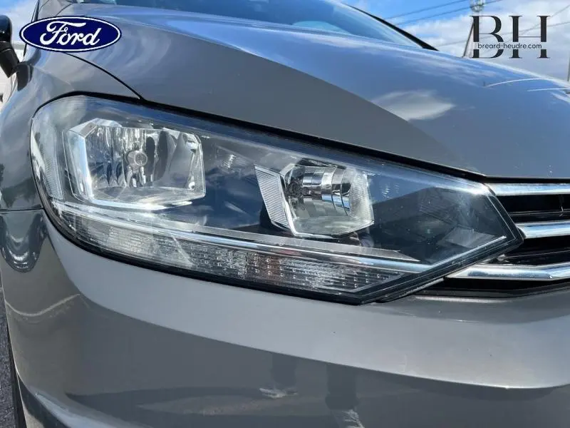 Gros plan sur le phare avant gauche du Volkswagen Touran gris Urano avec calandre chromée visible.