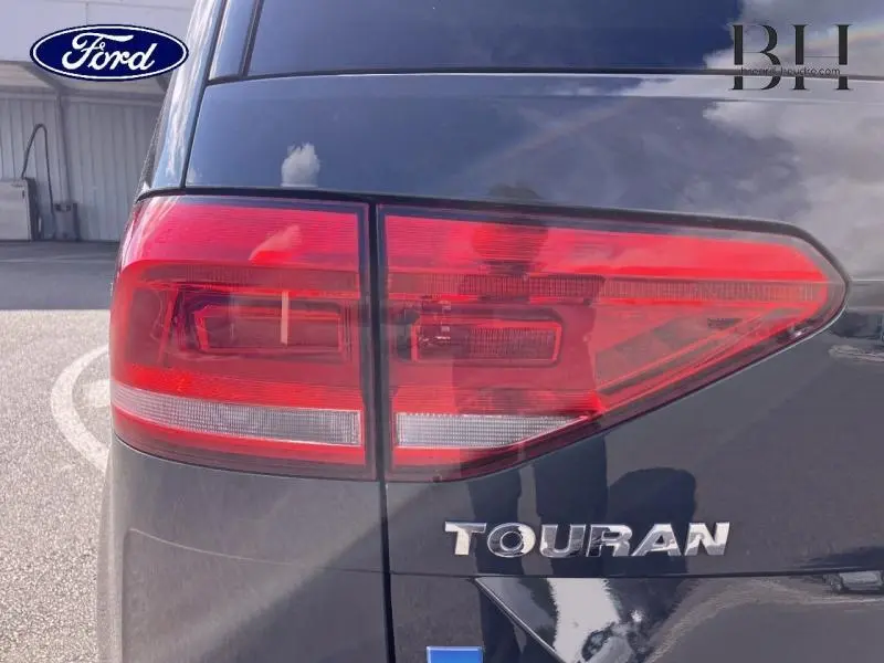 Gros plan sur le feu arrière droit d’un Volkswagen Touran gris Urano avec logo et nom du modèle visibles.