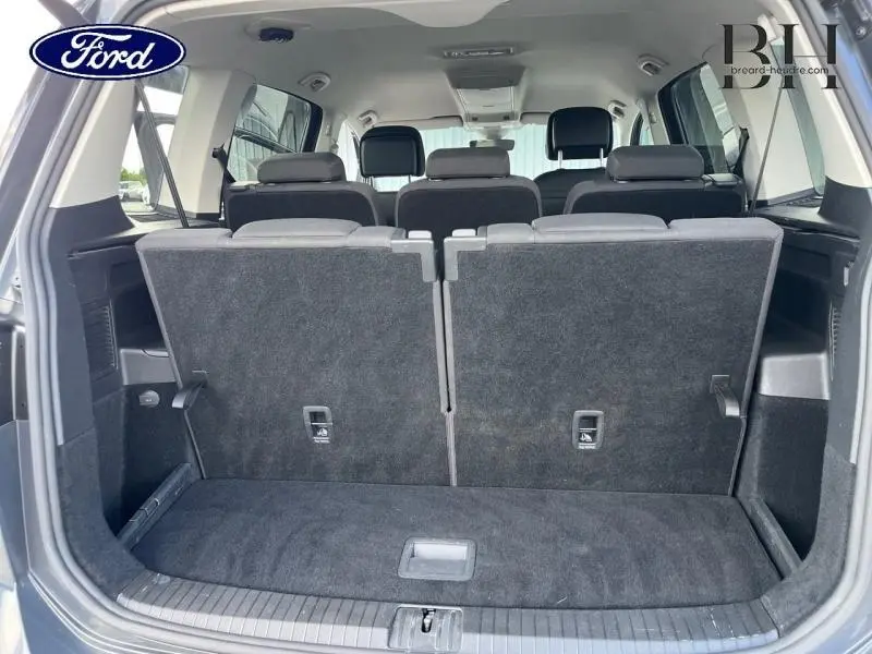 Vue arrière du coffre ouvert d'un Volkswagen Touran gris Urano, montrant la troisième rangée de sièges relevée et l'intérieur spacieux.