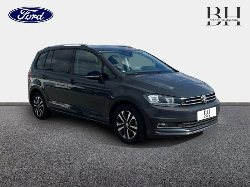 Volkswagen Touran gris Urano vu en 3/4 avant droit, avec jantes alliage et barres de toit visibles.