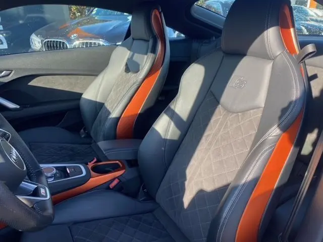 Intérieur de l'Audi TT 40 TFSI 2021 vu côté conducteur, sièges sport gris avec surpiqûres orange et logo S embossé.