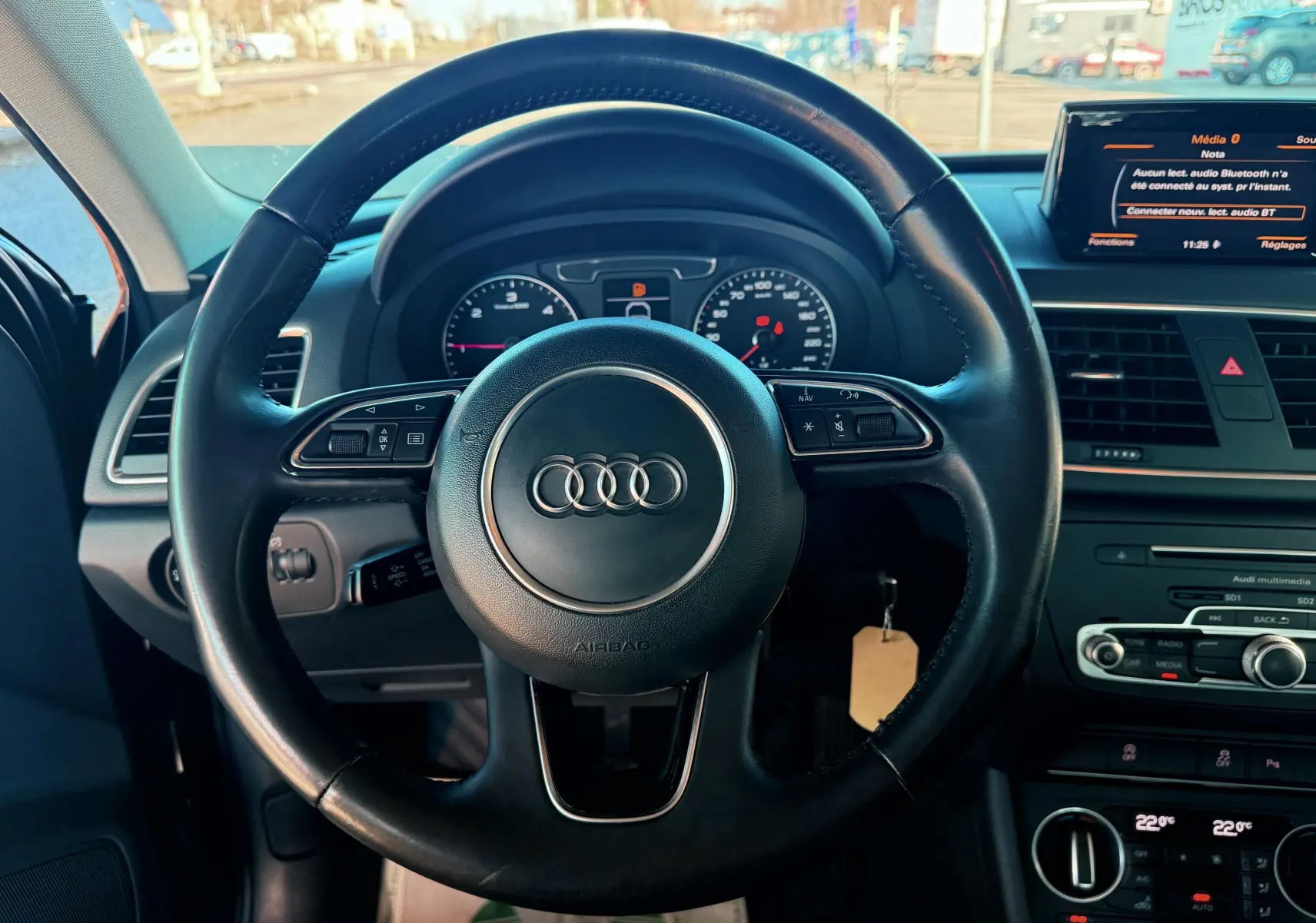 Vue intérieure centrée sur le volant noir d'un Audi Q3 2016 avec tableau de bord et écran multimédia visibles.