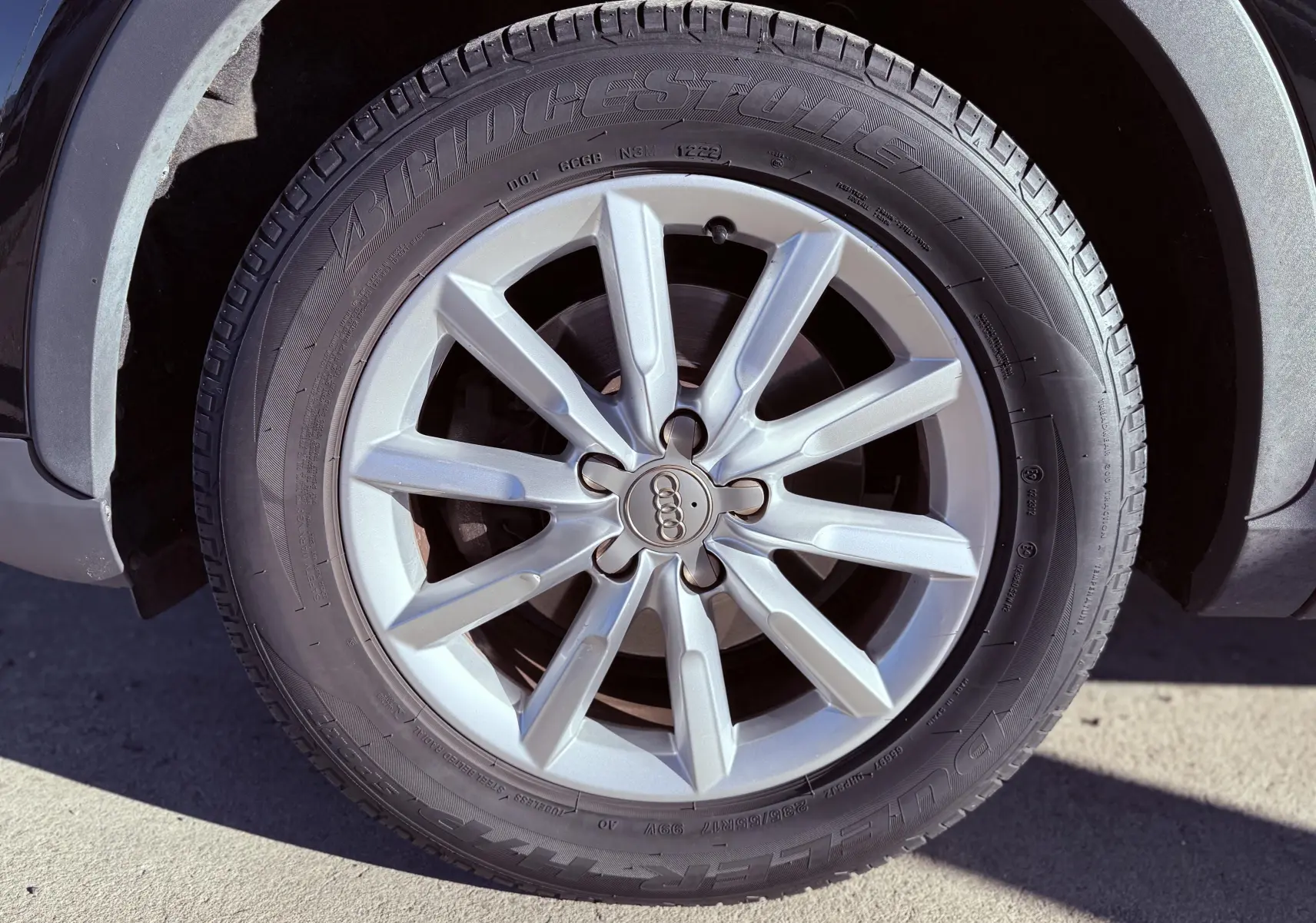Gros plan sur la jante argentée et le pneu Bridgestone du SUV Audi Q3 noir, mettant en valeur le logo Audi central.