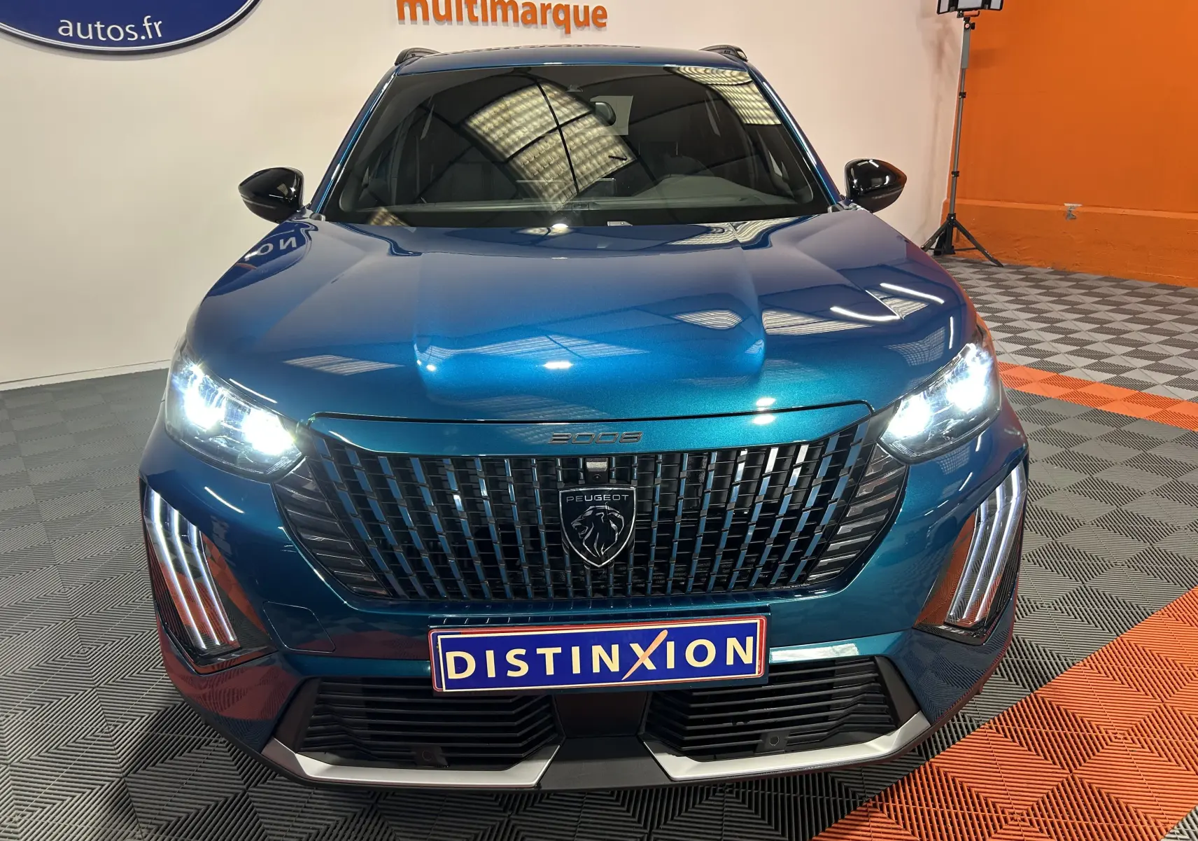Vue avant d'un Peugeot 2008 bleu Obsession avec phares allumés et calandre noire distinctive en intérieur showroom.