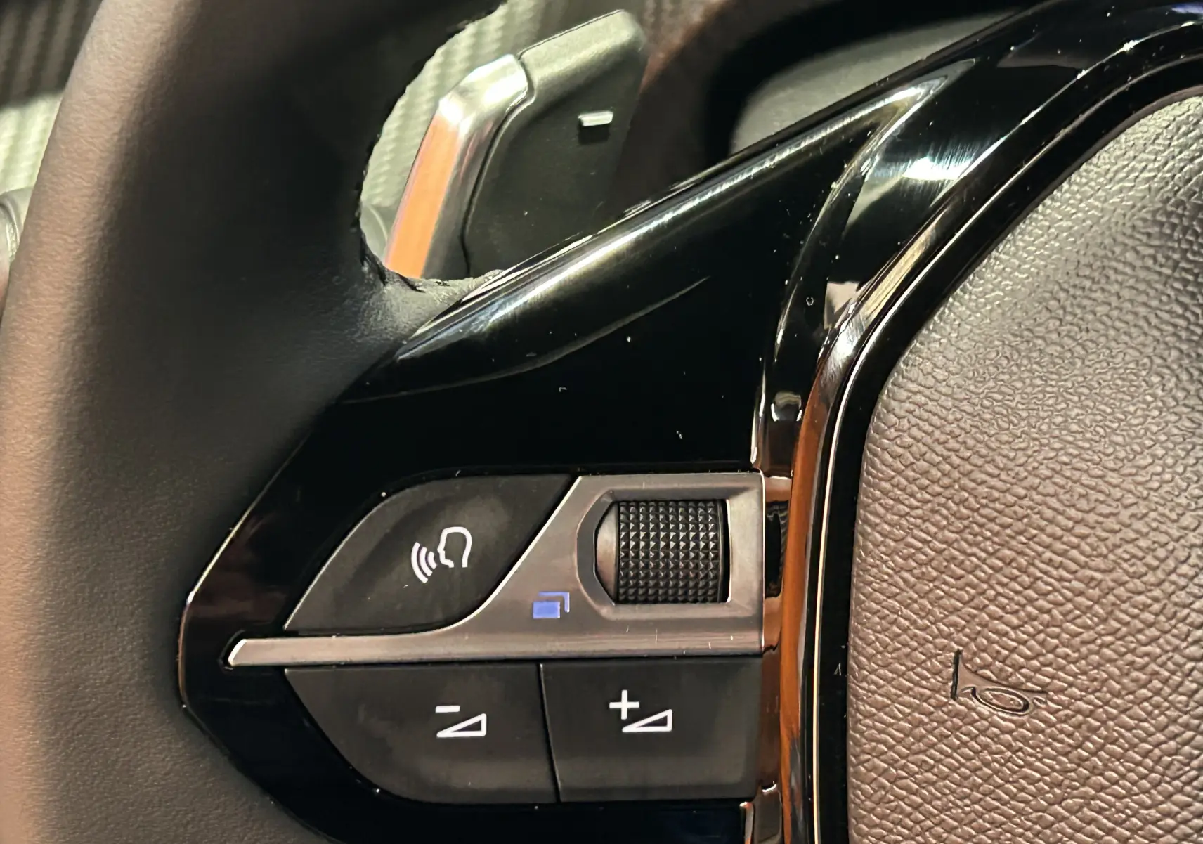 Gros plan sur les commandes vocales et volume au volant noir du Peugeot 2008 II Ph.2 Allure Hybrid 145 bleu Obsession.