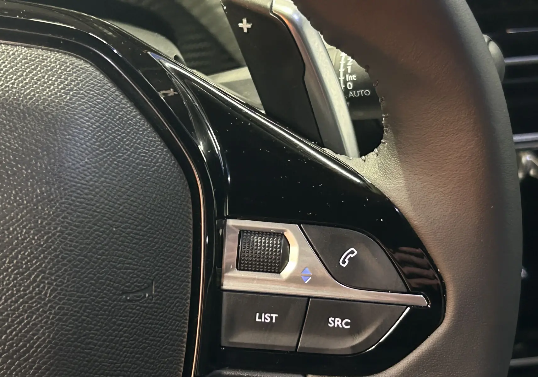 Gros plan sur les commandes du volant noir du Peugeot 2008 II Ph.2 Allure Hybrid 145, avec molette et boutons.