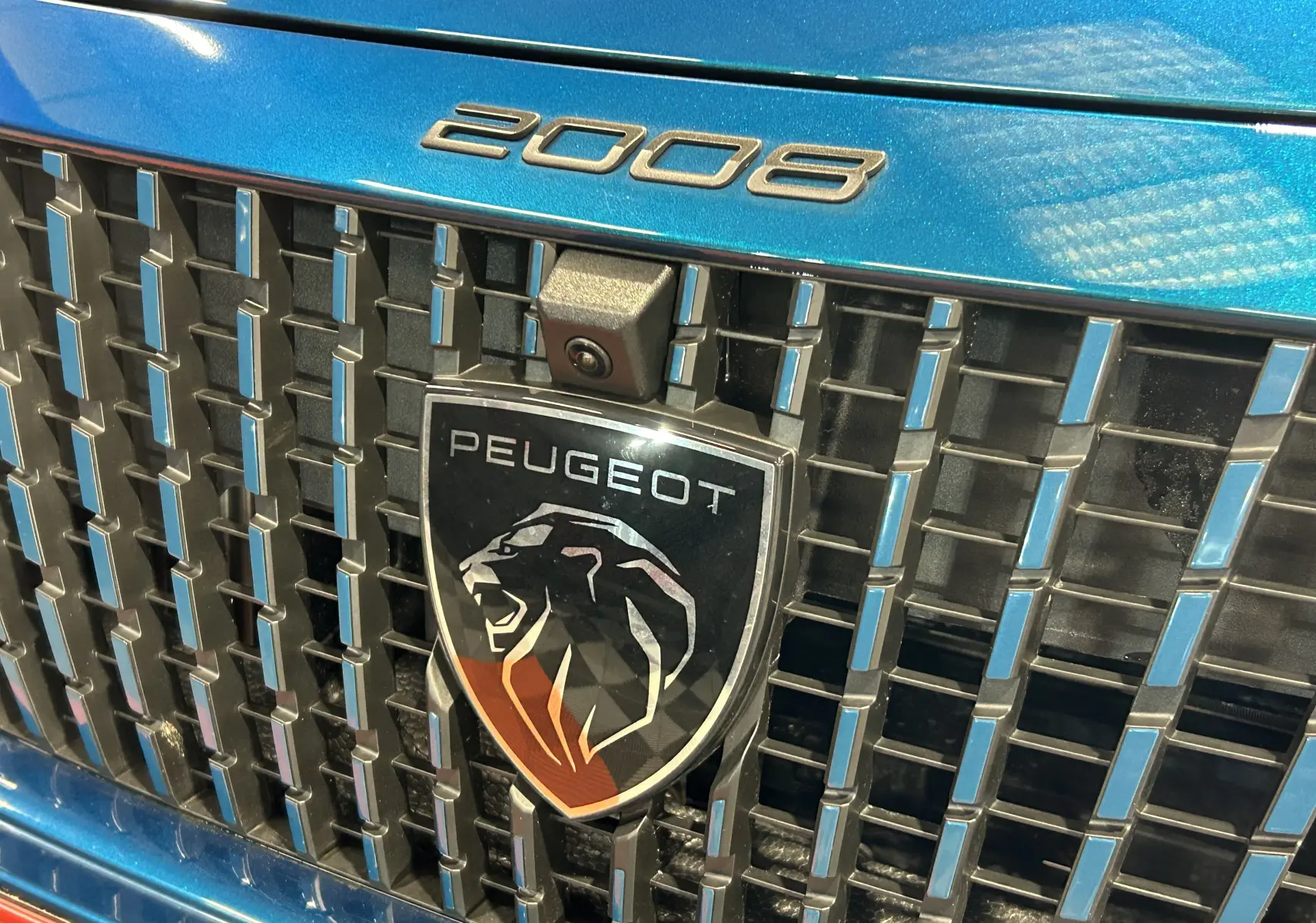 Gros plan sur la calandre bleue Obsession du Peugeot 2008 avec logo lion et caméra frontale intégrée.
