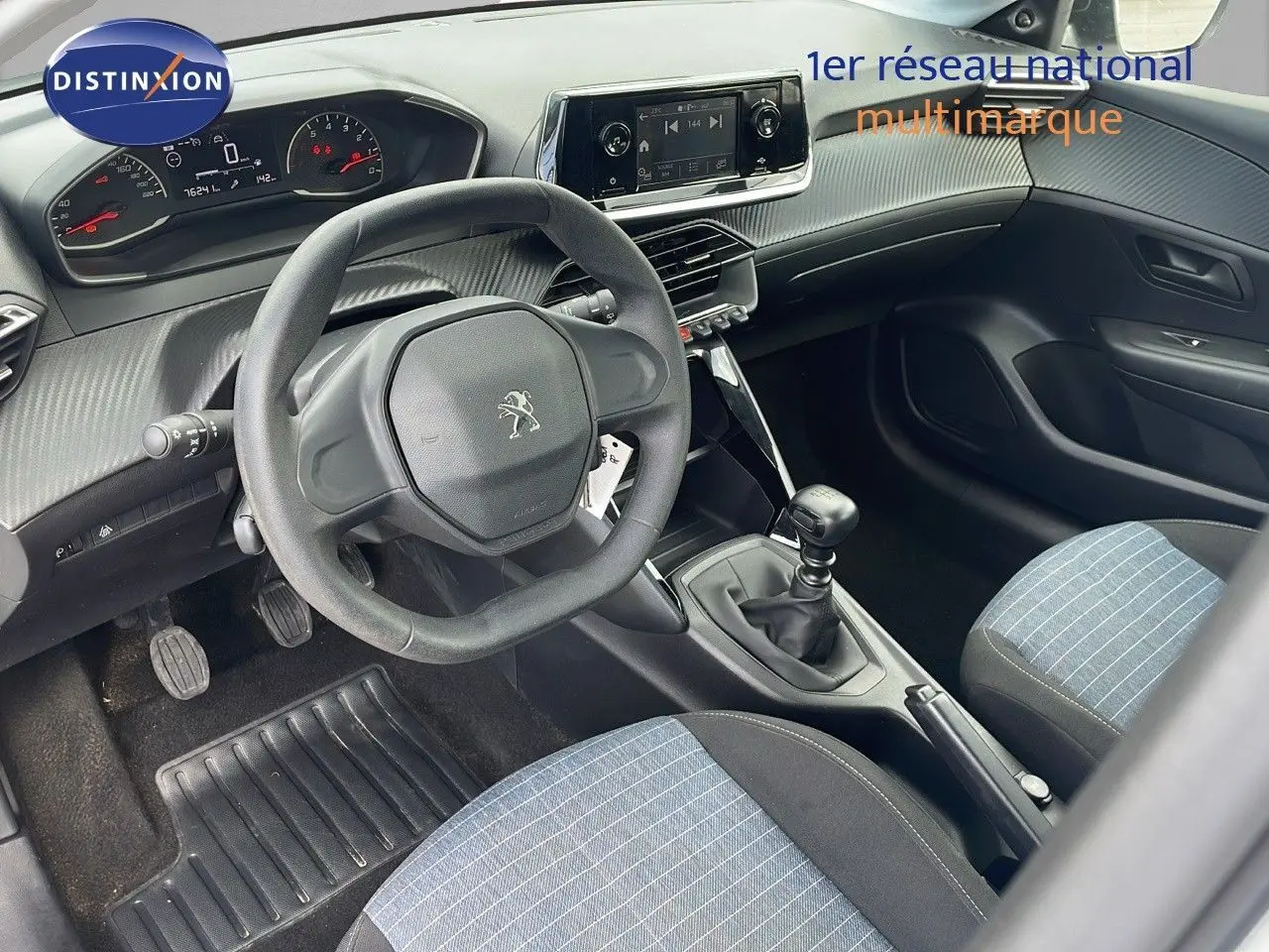 Vue intérieure côté conducteur du Peugeot 208 blanc banquise 2021, volant compact et sièges tissu bleu noir rayé.