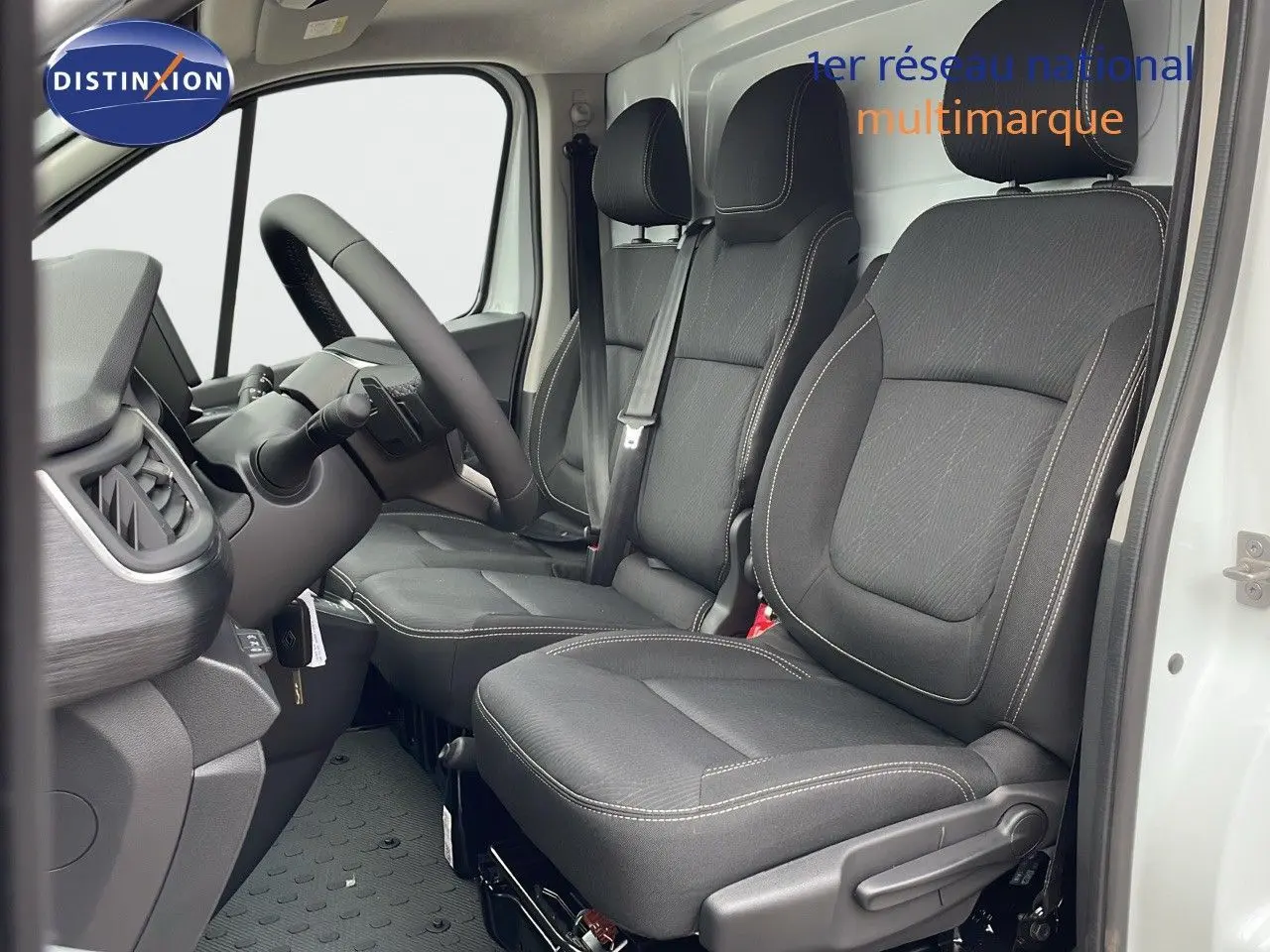 Intérieur avant du Renault Trafic Fourgon blanc glacier 2025, sièges noirs avec surpiqûres blanches et volant visible côté conducteur.